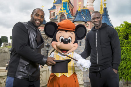 Teddy Riner et Omar Sy entourent l'apprenti magicien Mickey devant le Château de la Belle au Bois Dormant