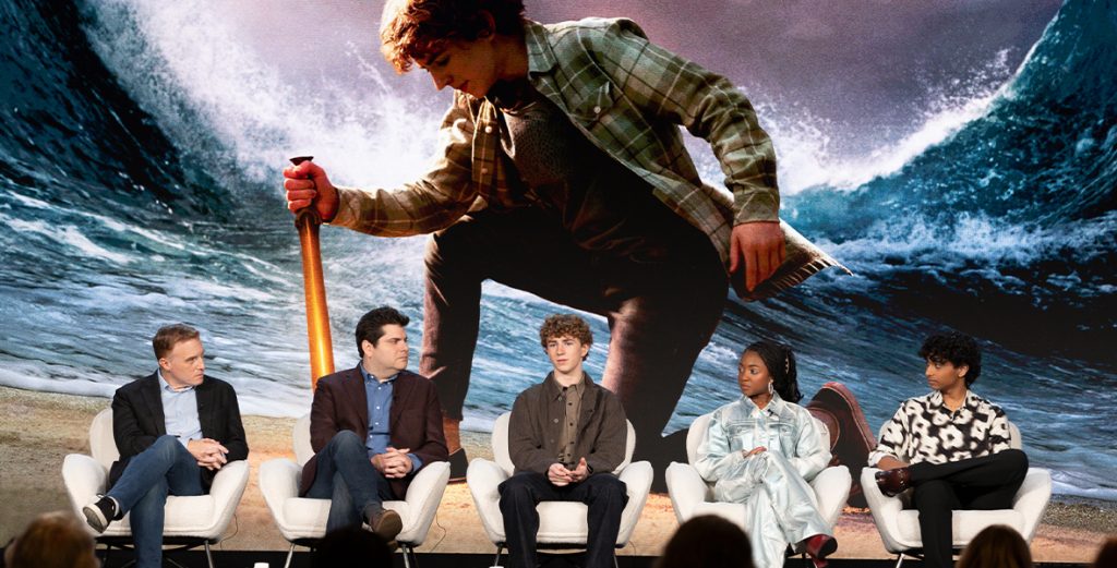 Un groupe de personnes assises sur des chaises devant une grosse vague lors de la deuxième saison de Percy Jackson.