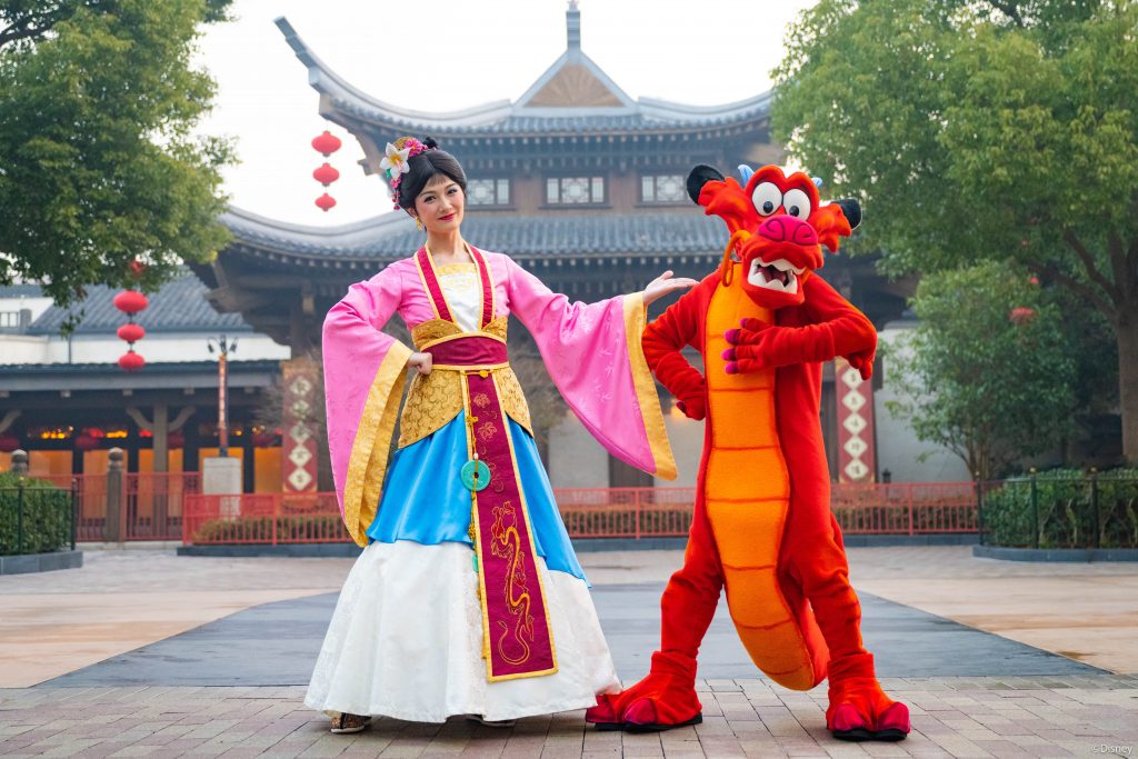 Une femme et une mascotte de dragon posant pour une photo à Shanghai Disneyland.