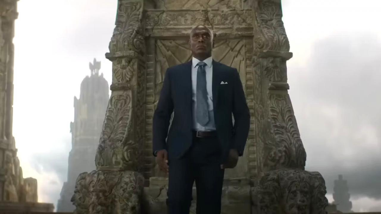 Un homme en costume debout devant un trône orné, rappelant une scène de "Percy Jackson : Saison 2.