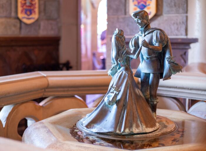 Statue en bronze d'un couple dansant au premier plan avec des bannières héraldiques floues en arrière-plan à Disneyland Paris.