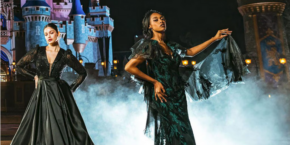 Deux femmes vêtues de robes élégantes posent de façon spectaculaire devant un château éclairé la nuit, capturant l'essence des méchants Disney avec un effet brumeux autour d'elles.