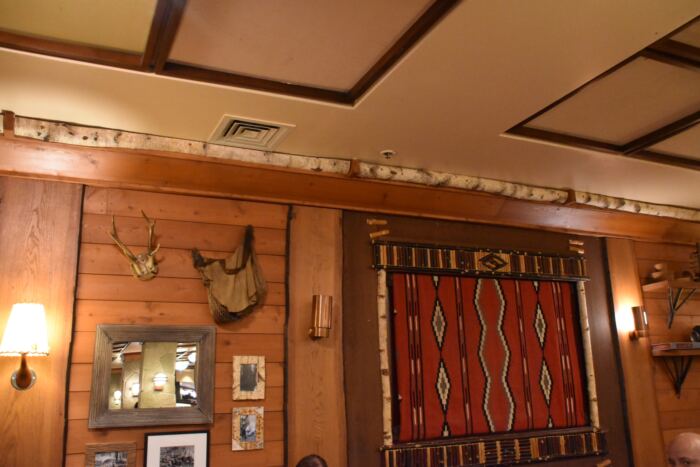 Un mur intérieur en bois avec des bois montés, un tapis à motifs rouges et noirs, des tableaux encadrés, une applique murale et une décoration d'étagère.