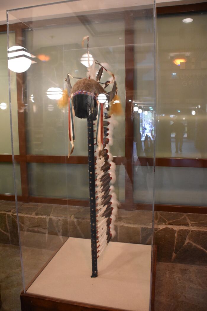 Une coiffe amérindienne avec un long panache de plumes est exposée dans une vitrine dans un musée ou une exposition.