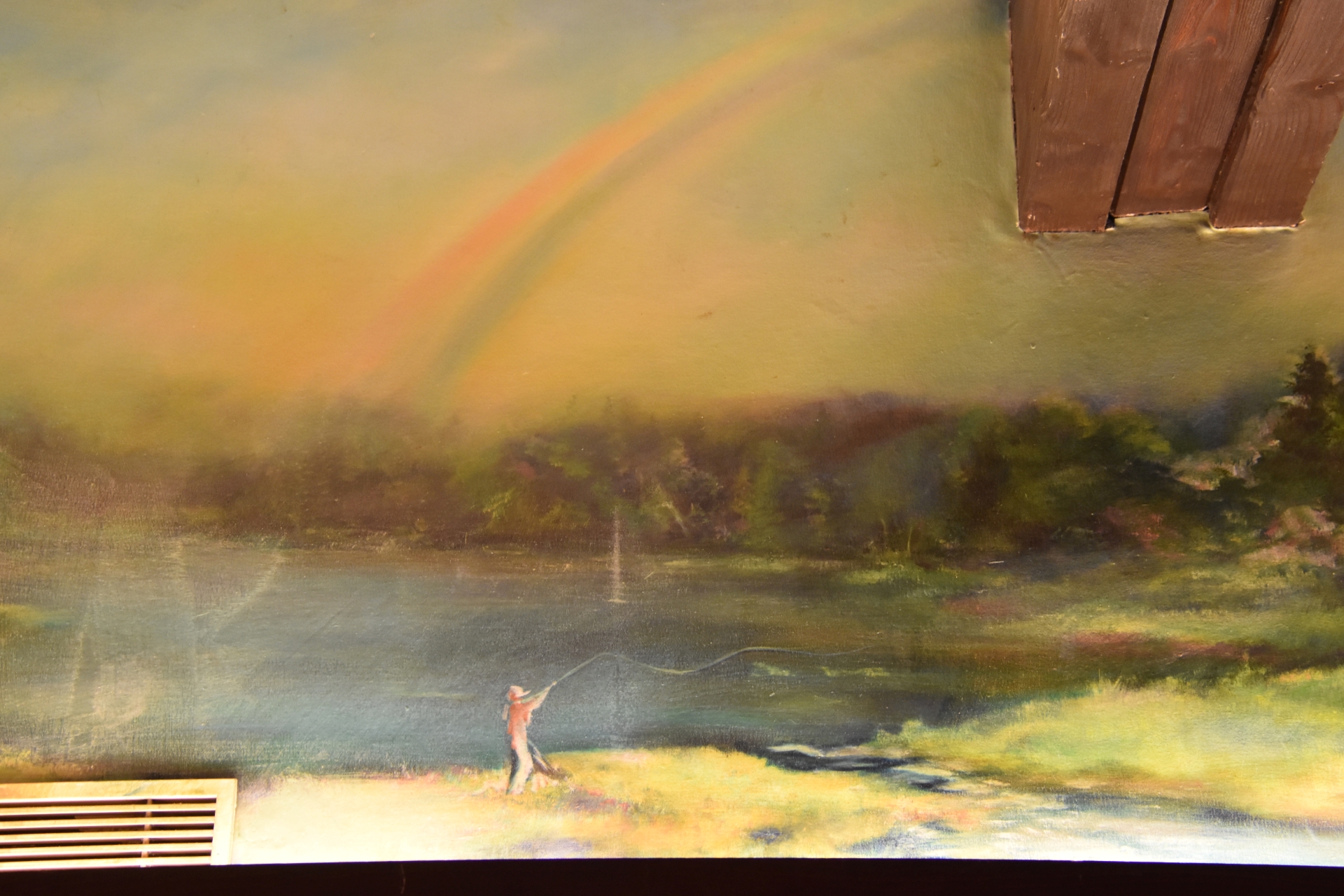 Une peinture représente une personne pêchant au bord d’un lac sous un arc-en-ciel, avec un fond d’arbres et un ciel nuageux.