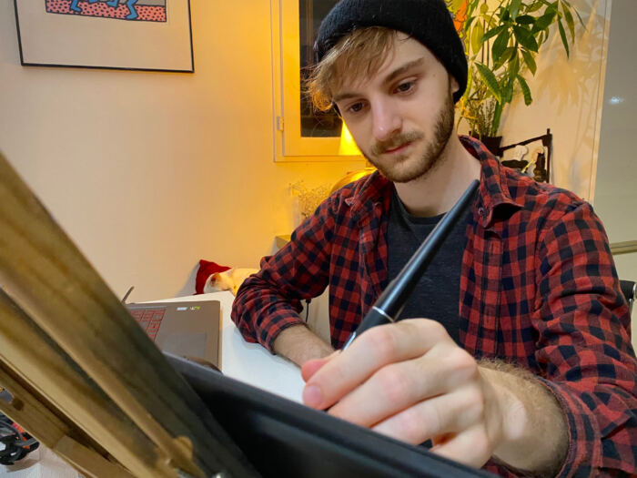 Une personne en chemise à carreaux et bonnet utilise un stylet sur une tablette à un bureau, plongée dans le montage d'un film. Un ordinateur portable bourdonne à côté d'eux, entouré de plantes en pot qui confèrent à l'image un air de tranquillité rappelant le charme étrange de Phantom Manor.