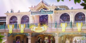 Entrée de Disneyland Paris avec une architecture ornementée, des bannières colorées et des passants. La lumière du soleil tombe à flot, créant une atmosphère animée.